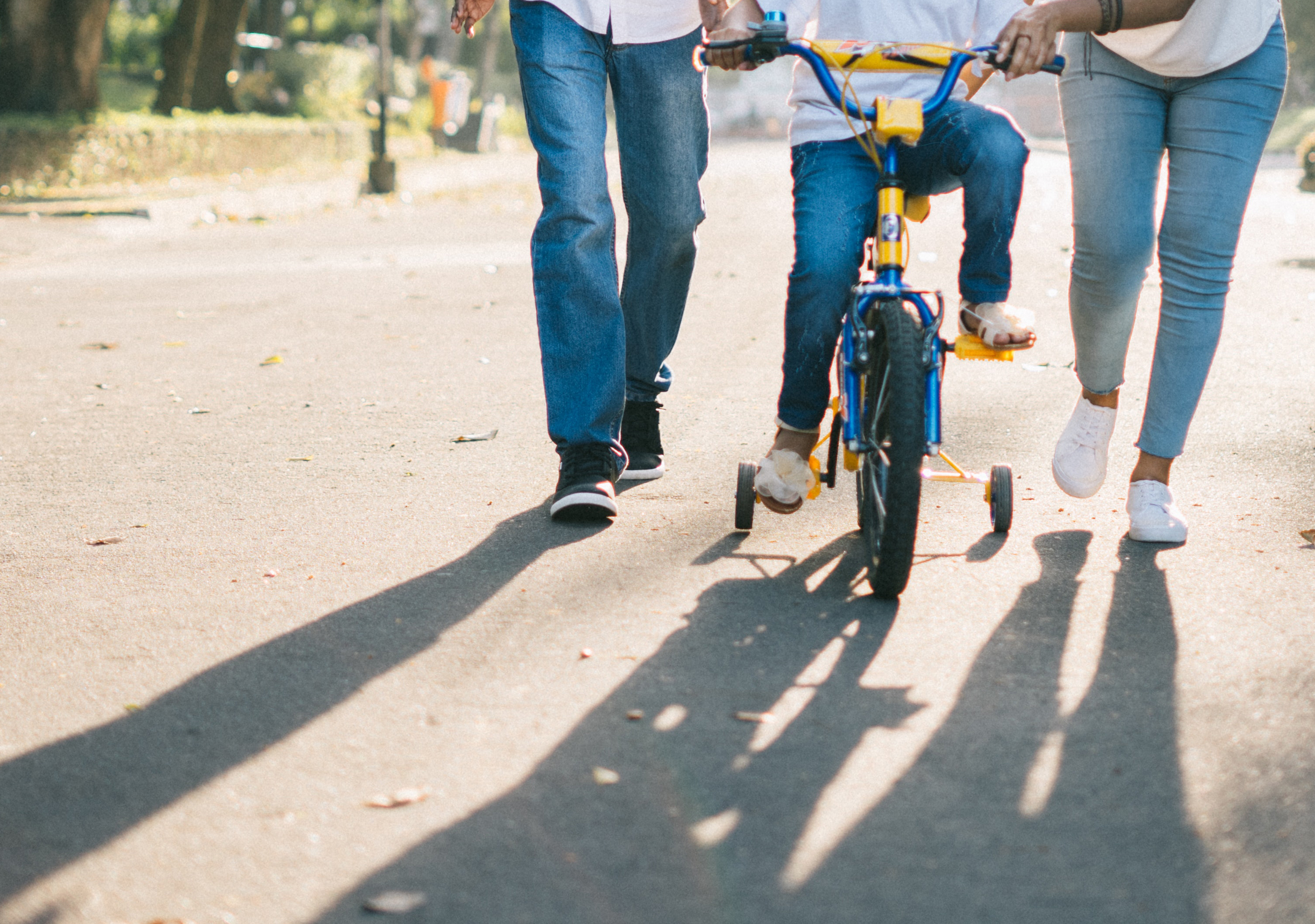 Two people help a child learn to ride a bicycle